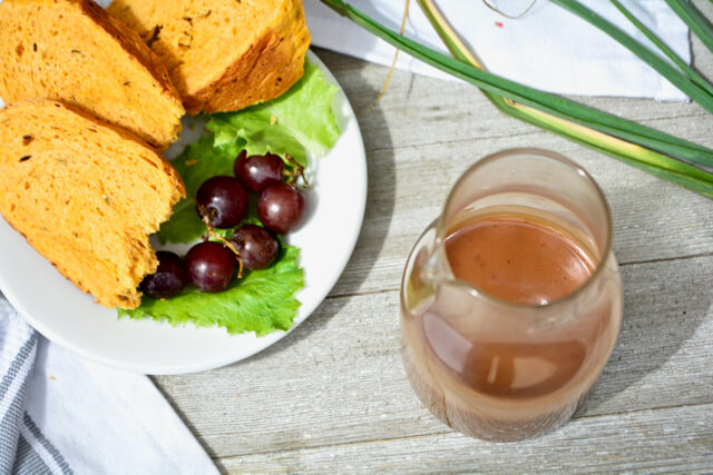 Overhead view of kidney friendly balsamic vinaigrette in a glass pitcher with a plate of grapes lettuce and bread
