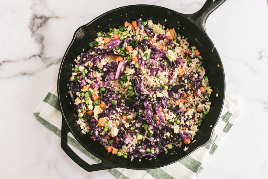 Low sodium cauliflower fried rice with purple cabbage and green onions in a black skillet on a marble counter. 