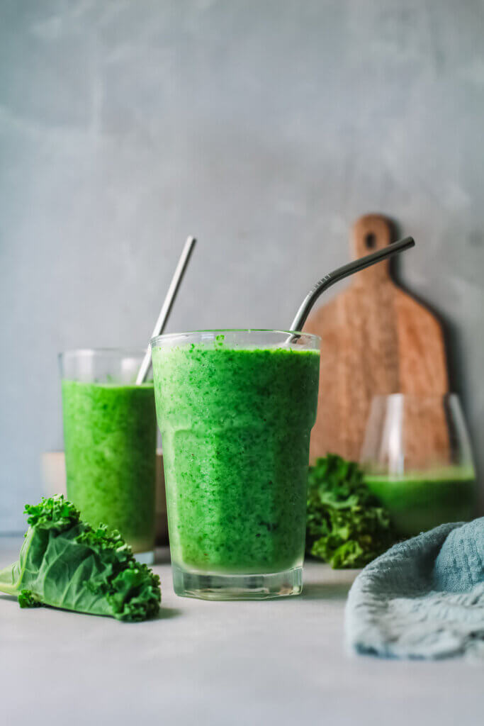 Front view green power smoothie with 3 glasses and wooden board with kale-CKD