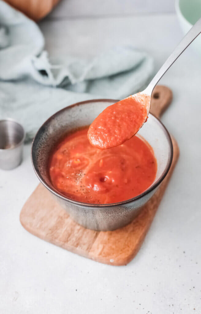 Roasted red pepper soup with spoon on a wooden board