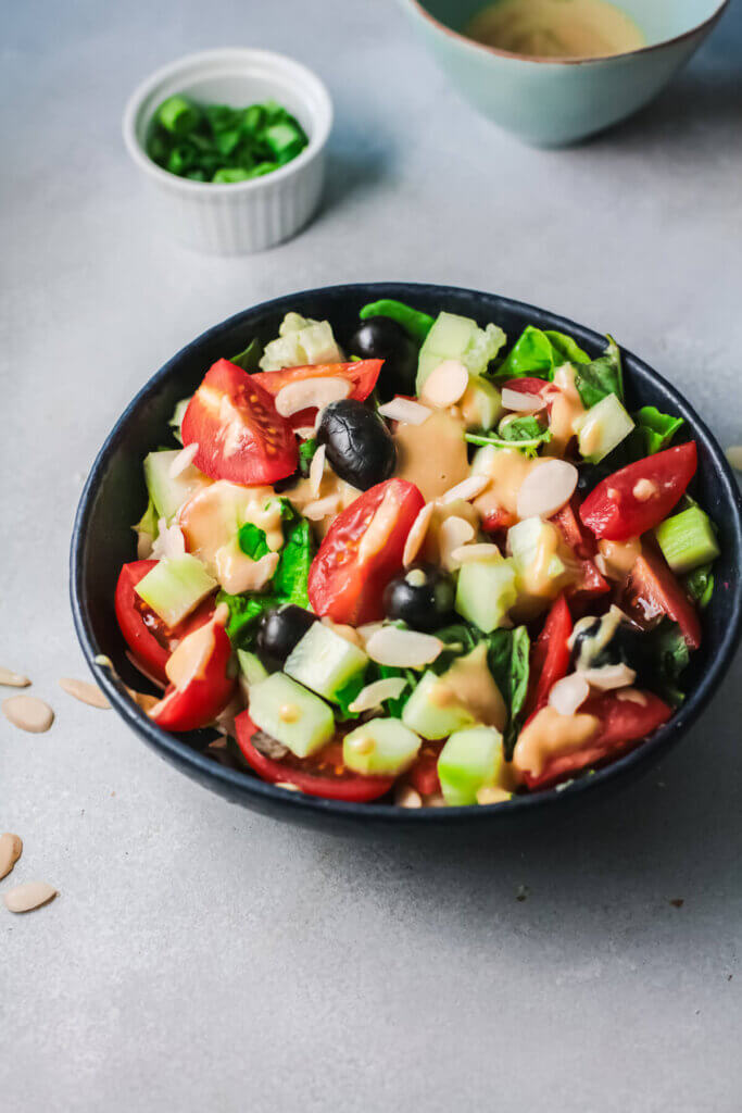Top angle view of tomato olive, tahini salad with bowl of green onions in a white bowl
