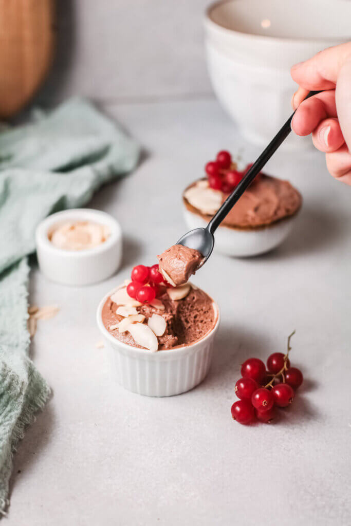 Coconut chocolate almond mousse in a white ramekin with a black spoon and berries
