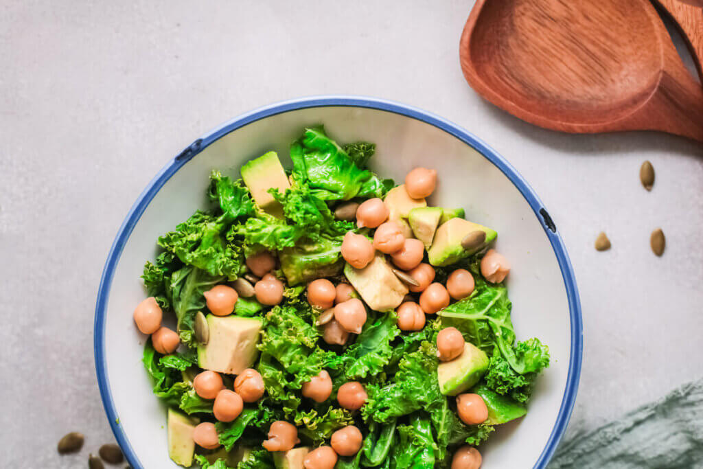 Overhead view of lemony kale salad with chickpeas in a white bowl with wooden spoon and green tea towel