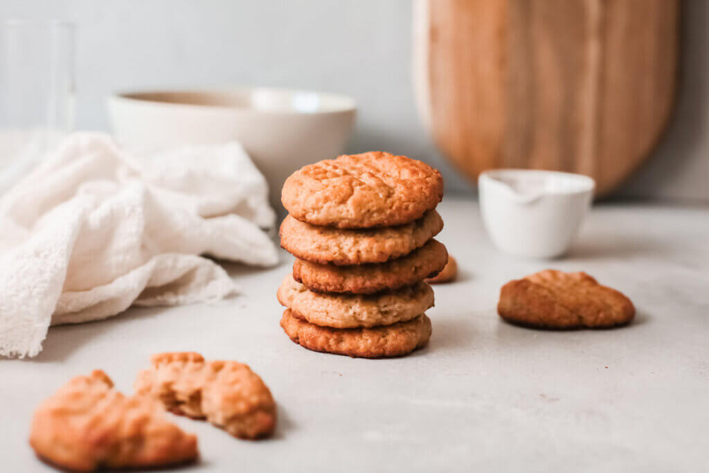 Stack of peanut butter maple cookies with white tea towel, white bowl and wooden board in the background