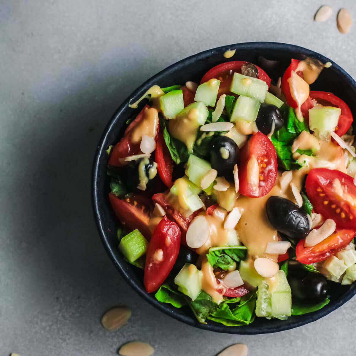 Top view olive, tahini and tomato salad with small dish of almonds