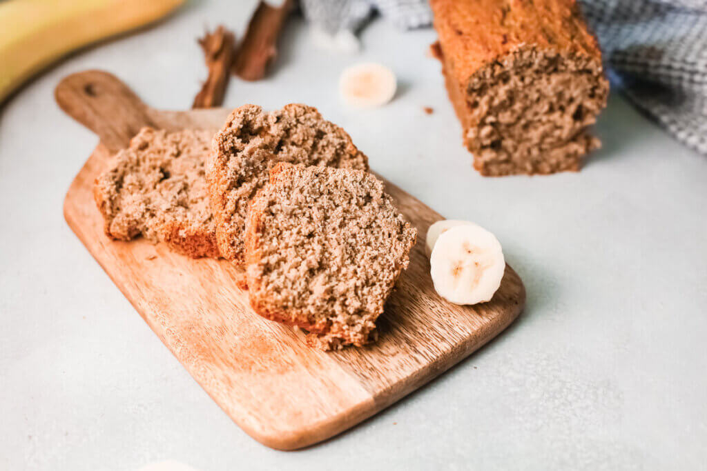 Vegan Banana Bread for Kidney Disease on a wooden cutting board with banana slices and cinnamon sticks and banana bread loaf 