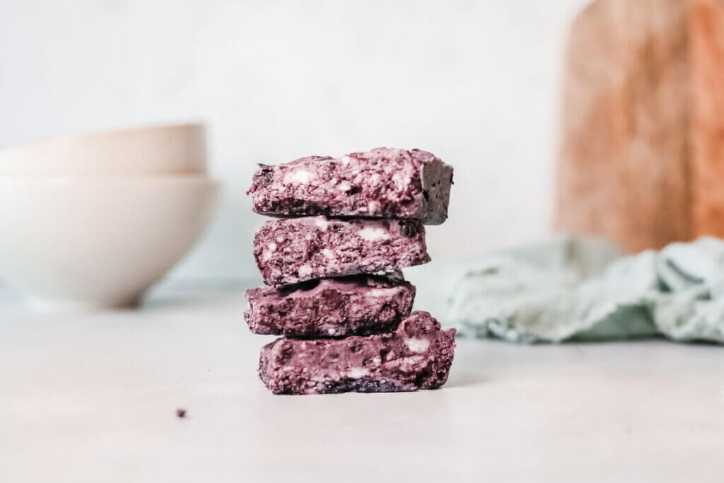 Stack of 4 Blackberry bliss bombs with two white bowls in the background and green tea towel and wooden board