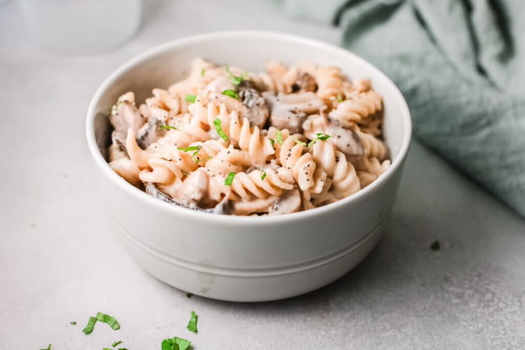 Side view of mushroom stroganoff in a white bowl with a green tea towel