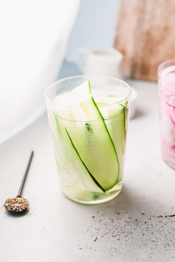 Close up view of quick pickled cucumbers with pickled red onions wooden spoon and wooden board in the background