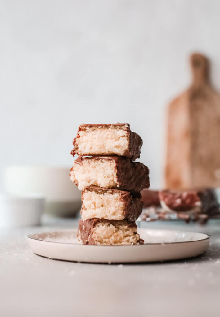 Stack of 4 vegan bounty bars on a white plate with small white bowls and wooden board in the background