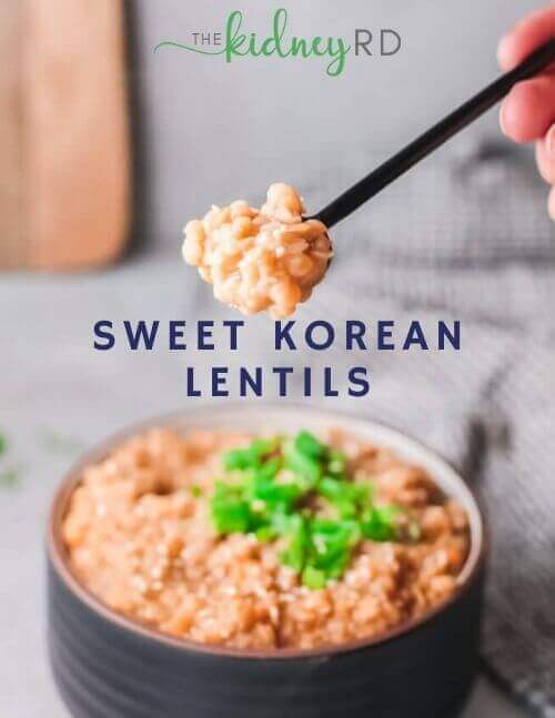 Black spoon filled with Sweet Korean lentils from black bowl topped with sliced green onions. Green tea towel and wooden cutting board in the background.