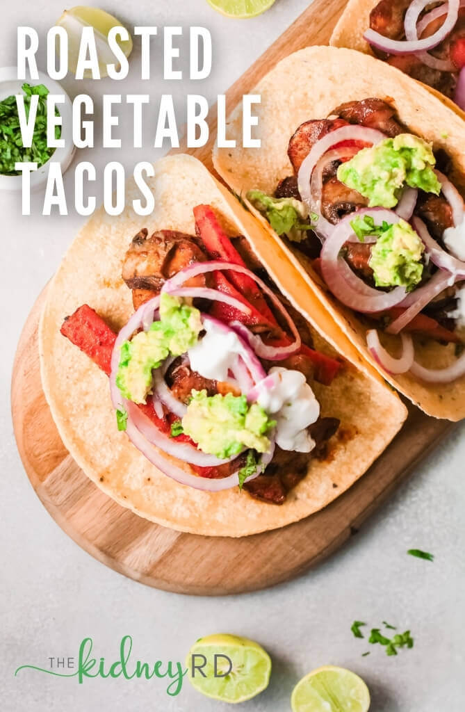 Top view marinated vegetable tacos on a wooden board with limes and small white bowl of cilantro