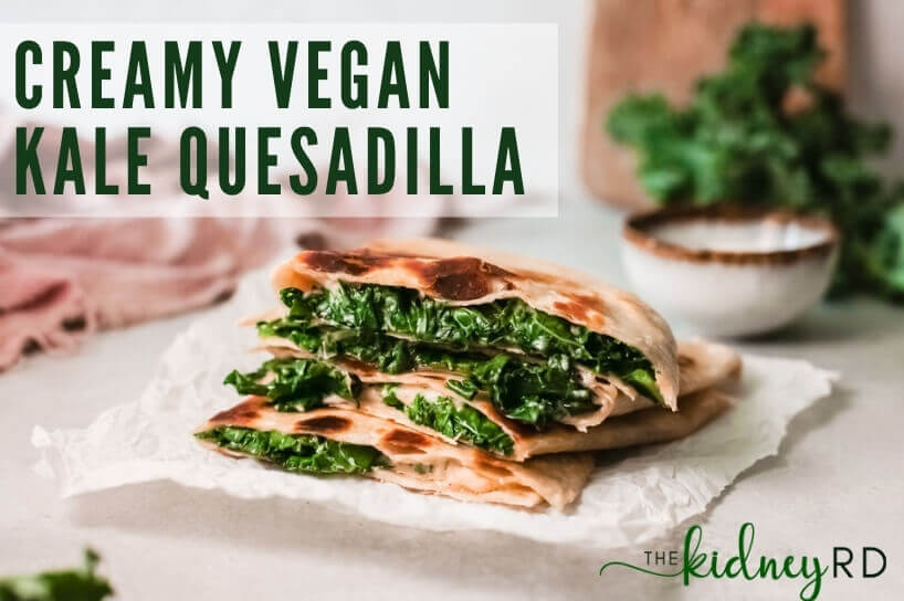 Side view of creamy kale vegan quesadilla quarters stacked on parchment with kale and small bowl of coconut yogurt and pink tea towel in background
