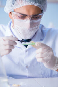 Close up view of man conducting research with a mask, lab coat, and hair net on examining a slide.