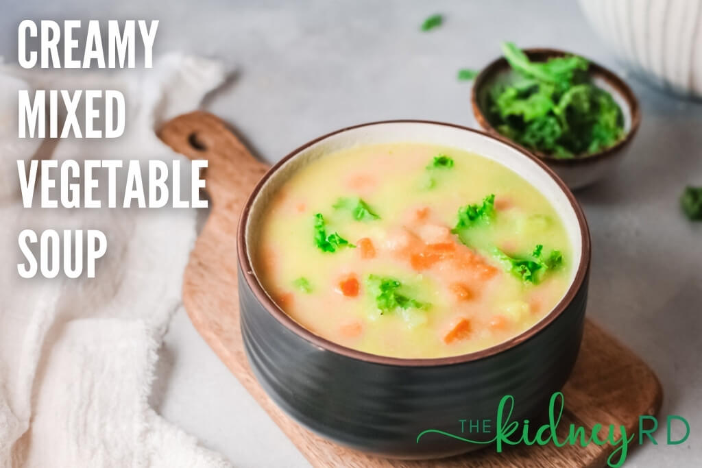 Low sodium creamy mixed vegetable soup in a black bowl with wooden spoon on a wooden board