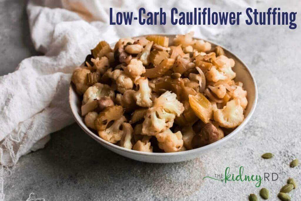 Side view of low carb cauliflower stuffing in a white bowl with a white tea towel and a pumpkin seeds sitting next to bowl