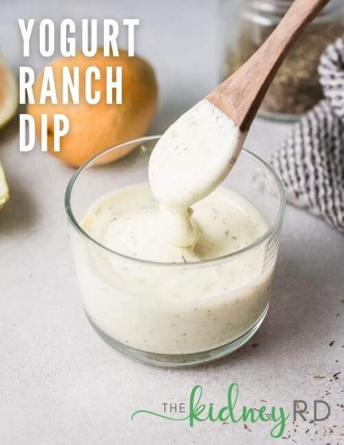 Overhead picture of Yogurt Ranch Dip and wooden spoon with lemons and black and white tea towel in the background.