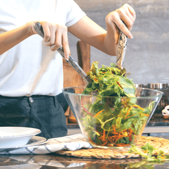 woman tossing a salad on a kitchen counter. Vegetable salad for CKD