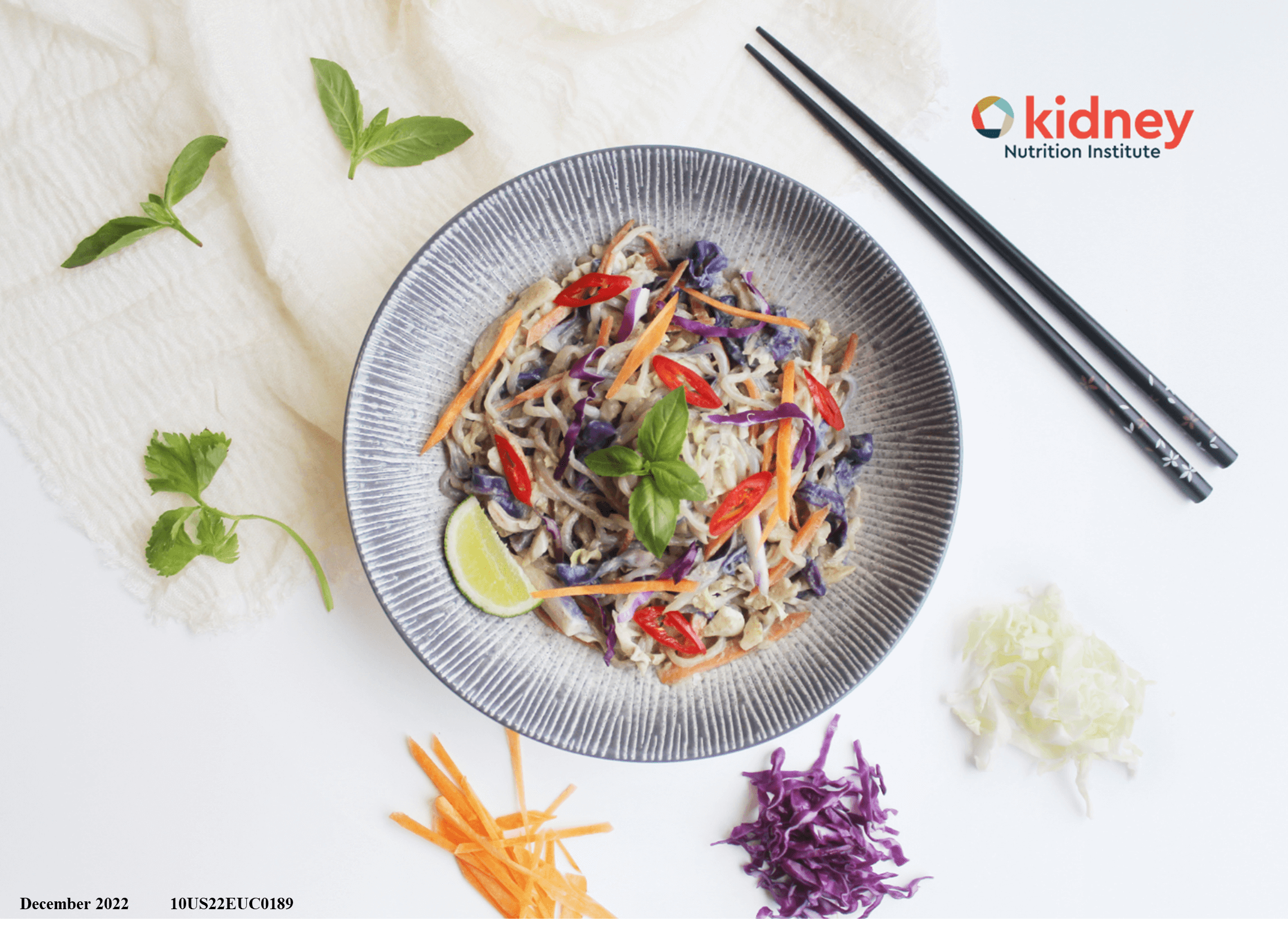 A bowl of Thai curry shirataki noodle stir fry with shredded green cabbage, purple cabbage, and carrot with a garnish of fresh basil and a wedge of lime