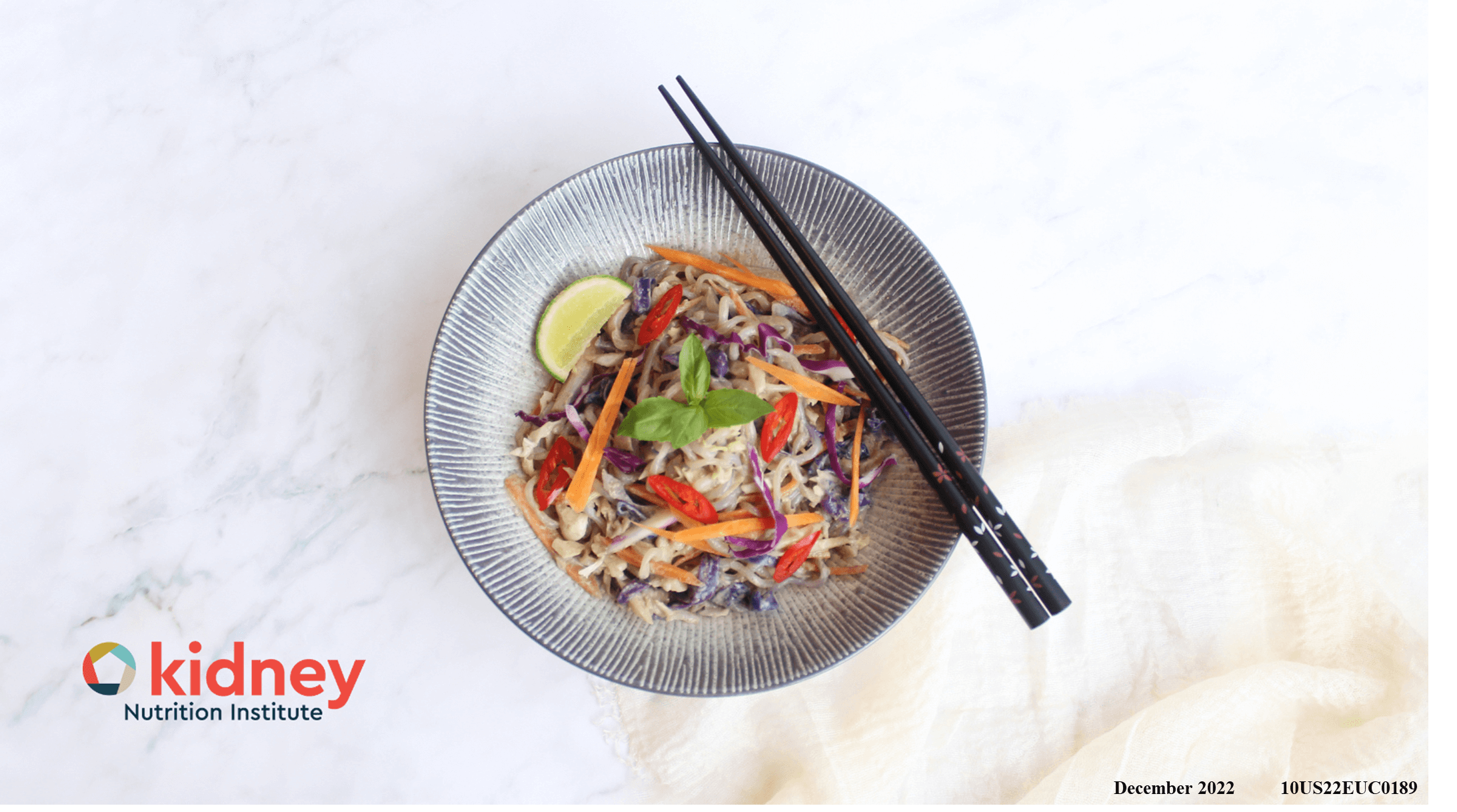 A bowl of Thai curry shirataki noodle stir fry with shredded green cabbage, purple cabbage, and carrot with a garnish of fresh basil and a wedge of lime
