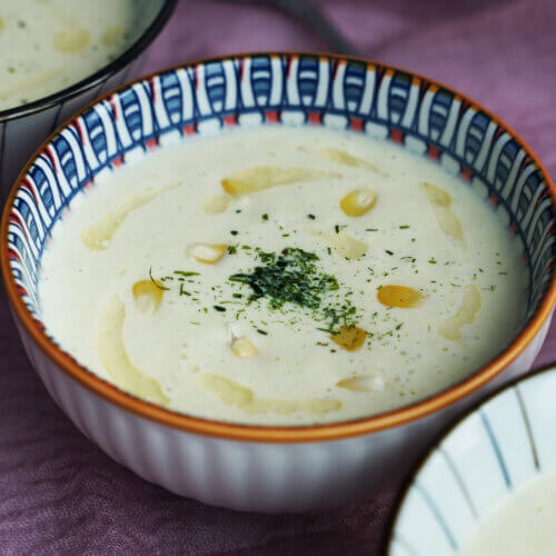 Three bowls of creamy corn soup with a drizzle of olive oil and parsley as garnish