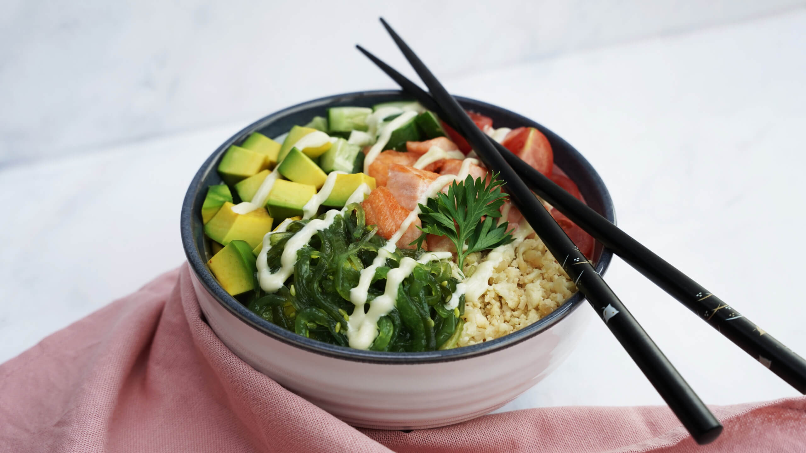 Keto Salmon Poke Bowl - a bed of cauliflower rice with cucumber, tomato, salmon, avocado, and seaweed topping, topped with a drizzle of spicy wasabi mayonnaise