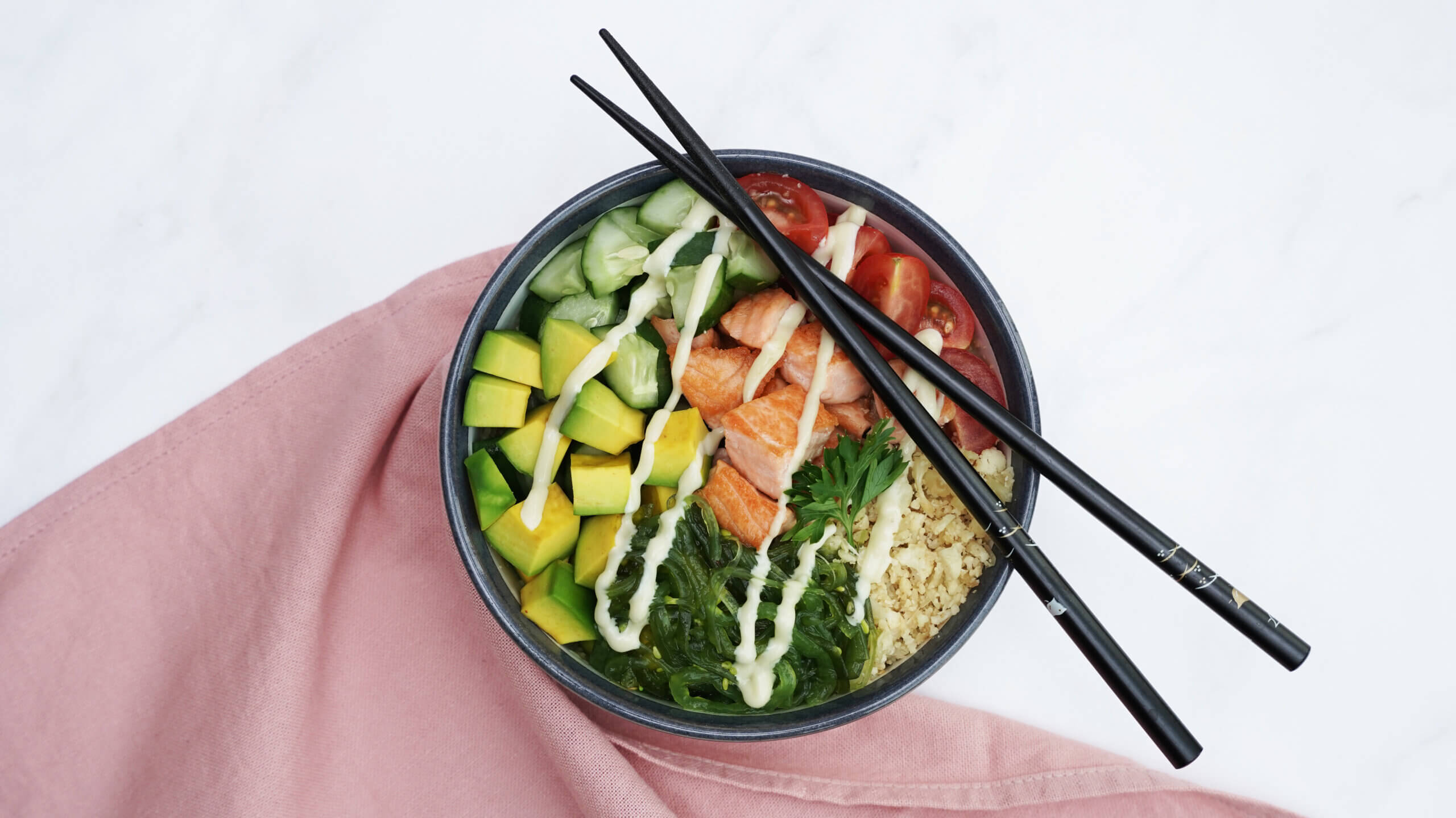 Keto Salmon Poke Bowl - a bed of cauliflower rice with cucumber, tomato, salmon, avocado, and seaweed topping, topped with a drizzle of spicy wasabi mayonnaise