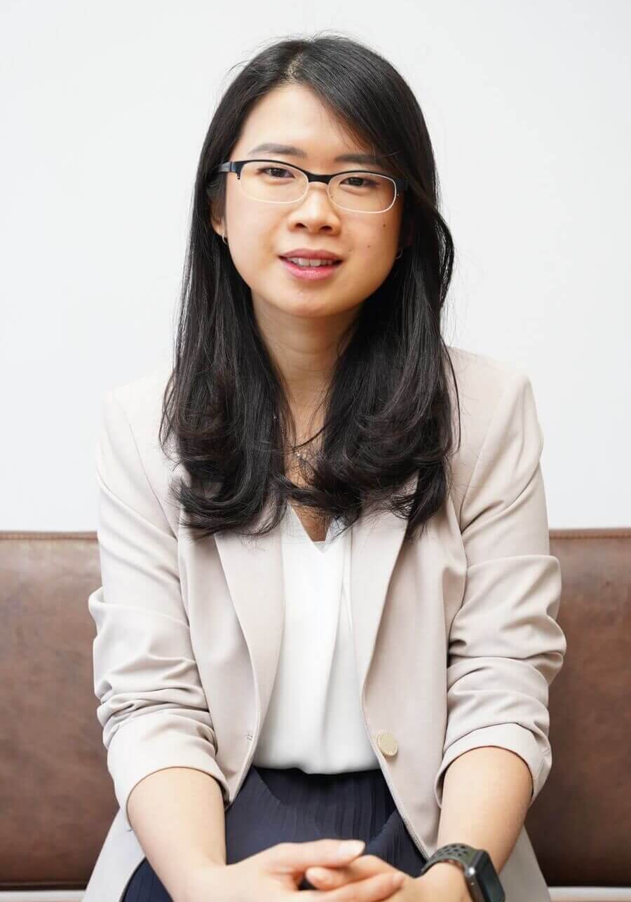 Asian woman with long dark hair and wire rimmed glasses in a beige blazer